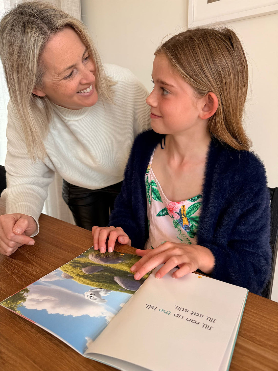 A teacher smiling warmly at a child during a decodable book reading session